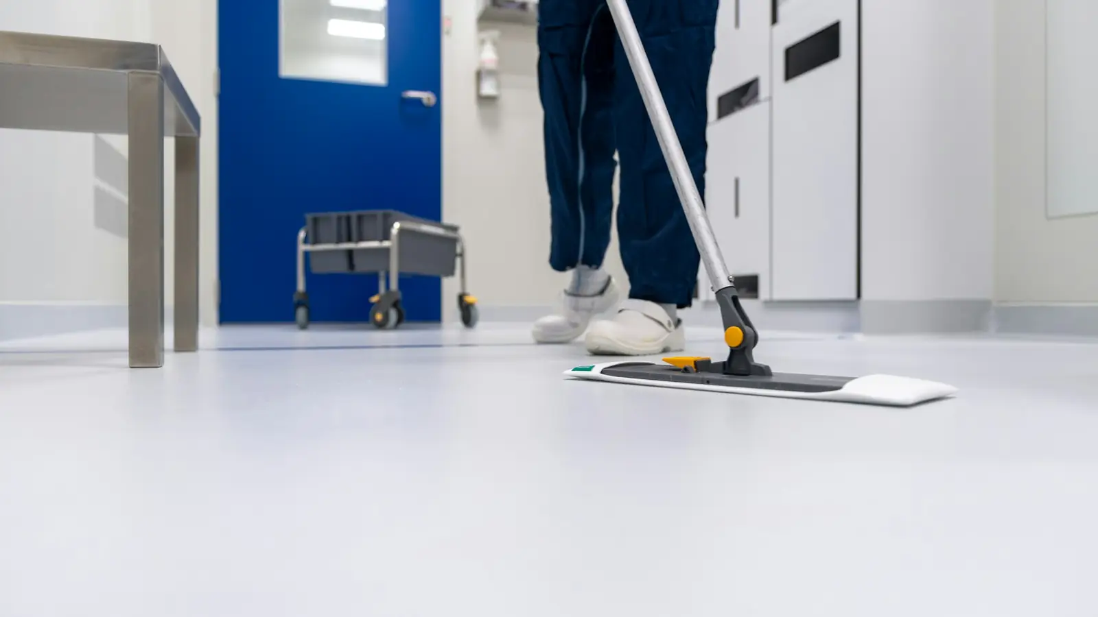 Schoonmaker dweilt de vloer van een steriele ruimte met een vlakmop